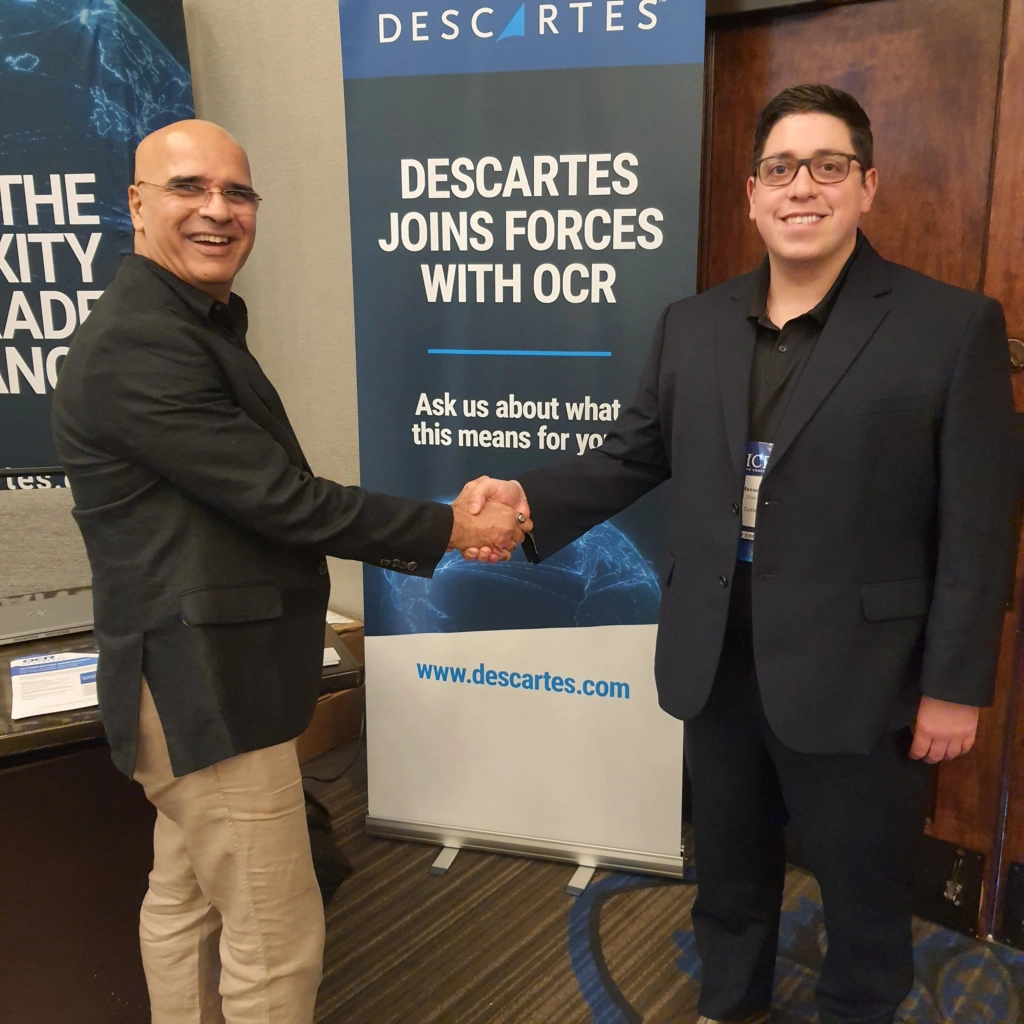 Two Descartes Export Compliance Experts at the 2024 ICPA ITAR Conference standing in front of a sign that reads ‘Descartes Joins Forces with OCR’ 